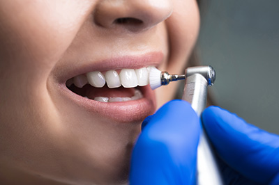 A person receiving dental care with a dental hygienist using an electric toothbrush and wearing blue gloves.