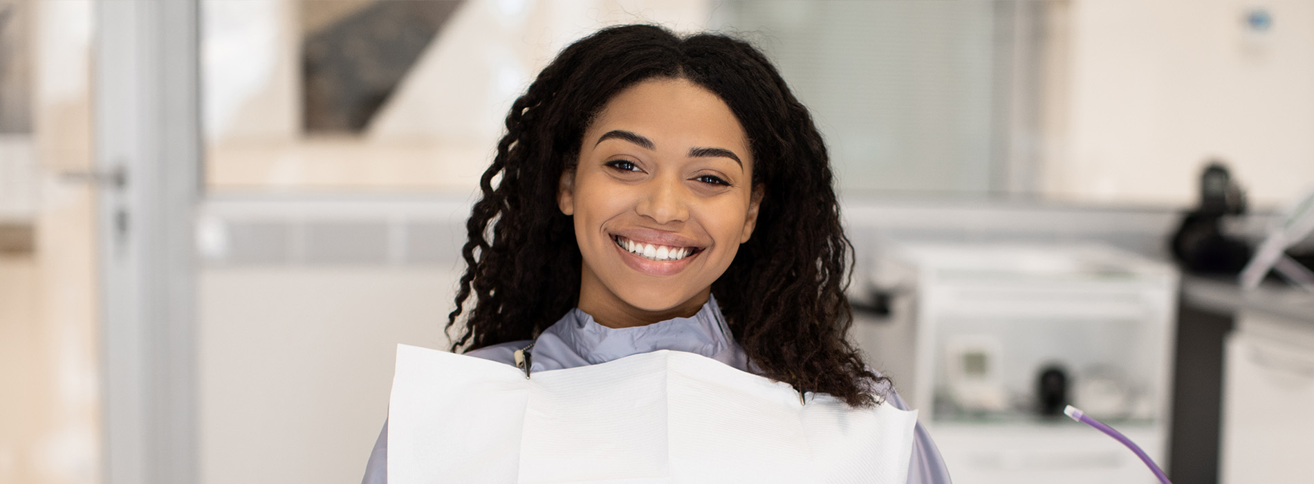 A young woman with a bright smile stands behind a dental chair, holding a dental model in her hands.