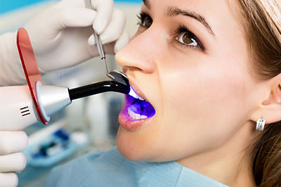 A woman receiving a dental cleaning, with a dental hygienist using a professional dental cleaning device.