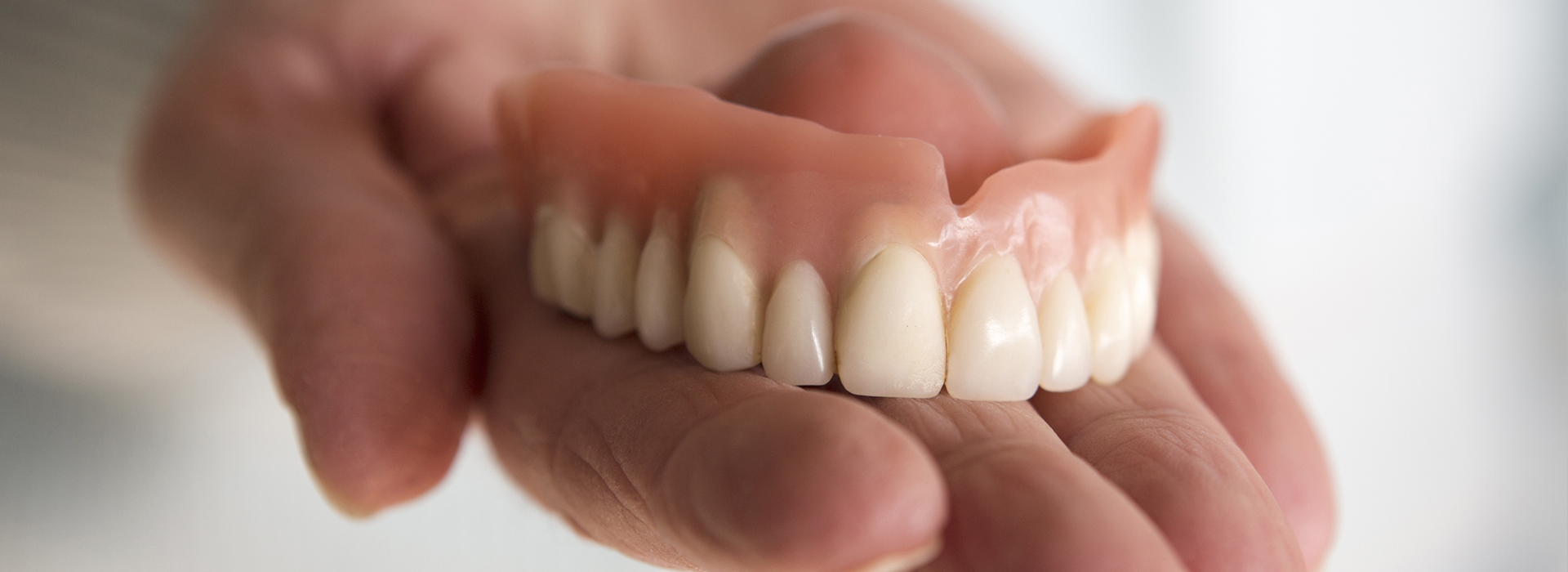A hand holding a set of dentures against a blurred background.