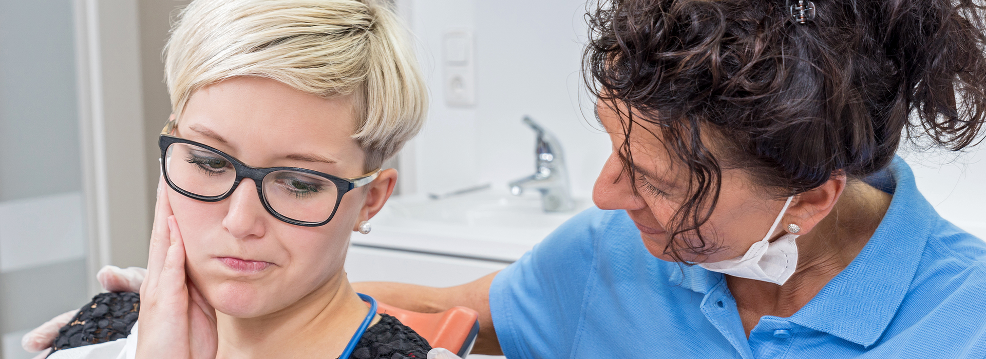 A woman with glasses is receiving a dental cleaning from a dentist, showcasing a professional dental care setting.