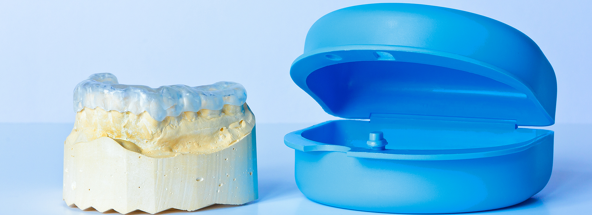 The image shows a blue dental implant next to a yellow model of a human mouth with teeth, likely for educational or sales purposes.
